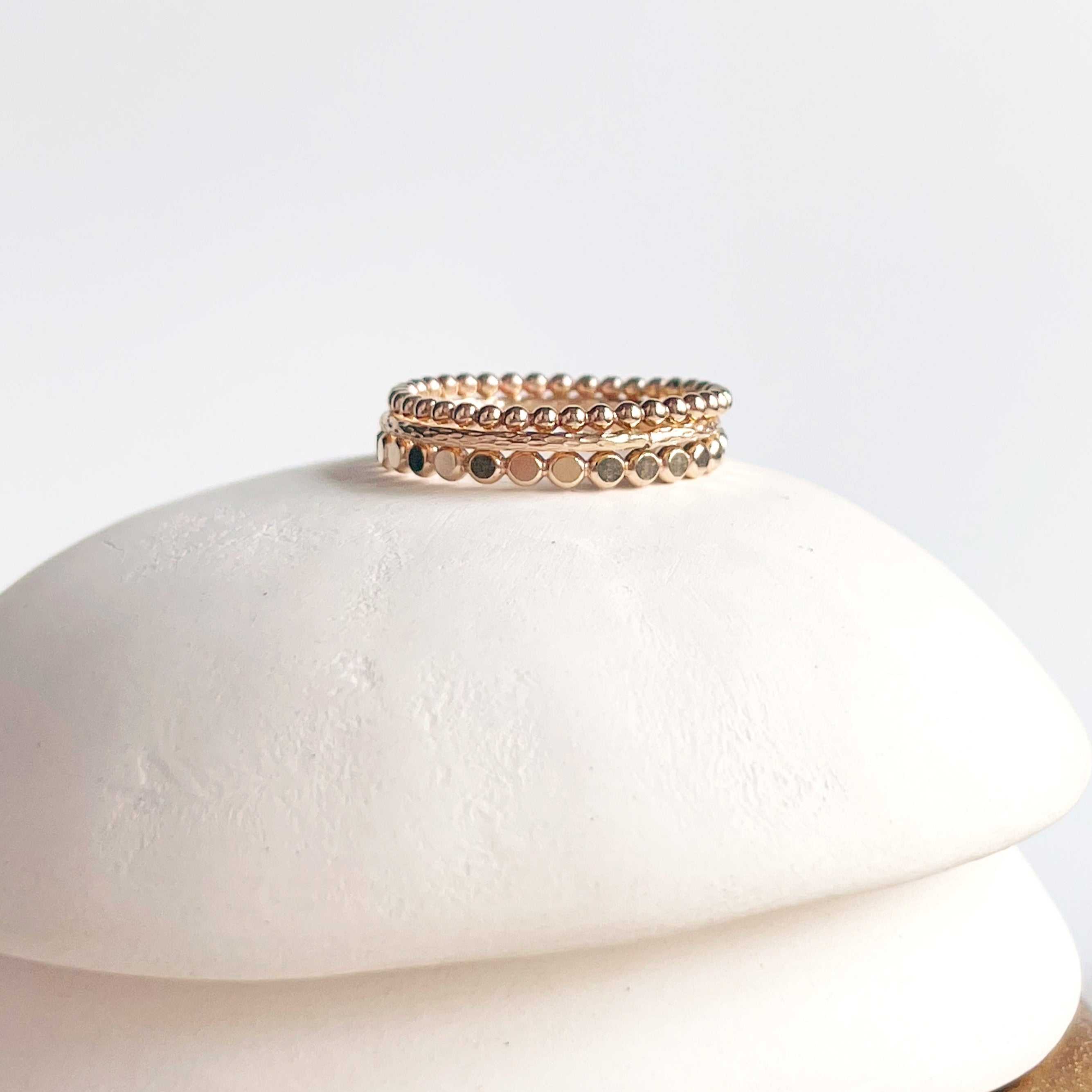 A stack of three gold beaded rings with a textured surface, displayed on a white marble surface.