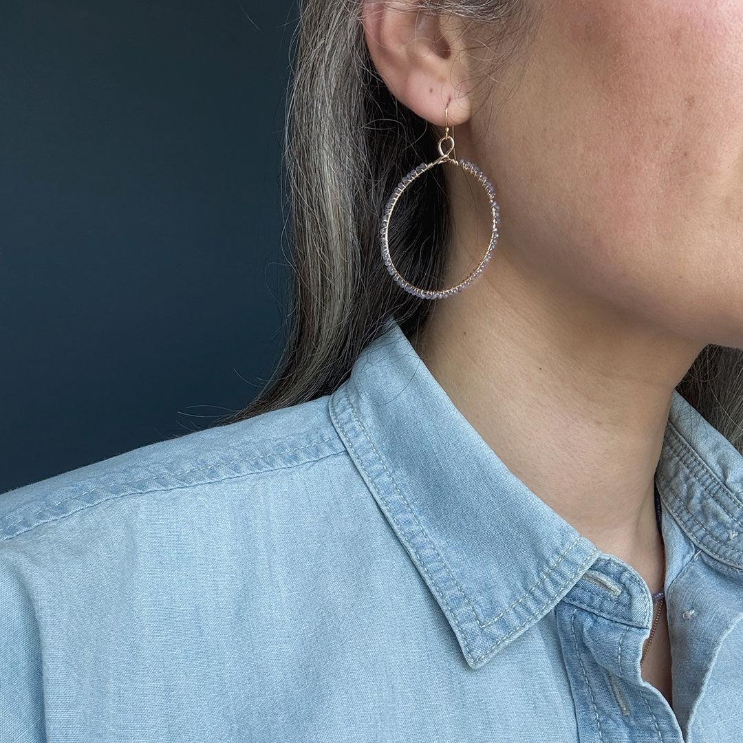 Close-up of a person wearing a hoop earring with small tanzanite stones on a dark background