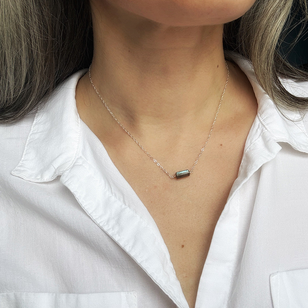 Necklace with a labradorite gemstone worn by a person in a white shirt