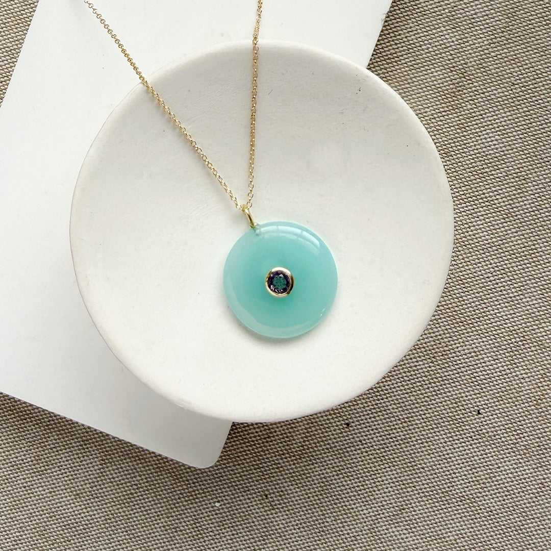 Round chalcedony pendant on a gold chain in a white dish