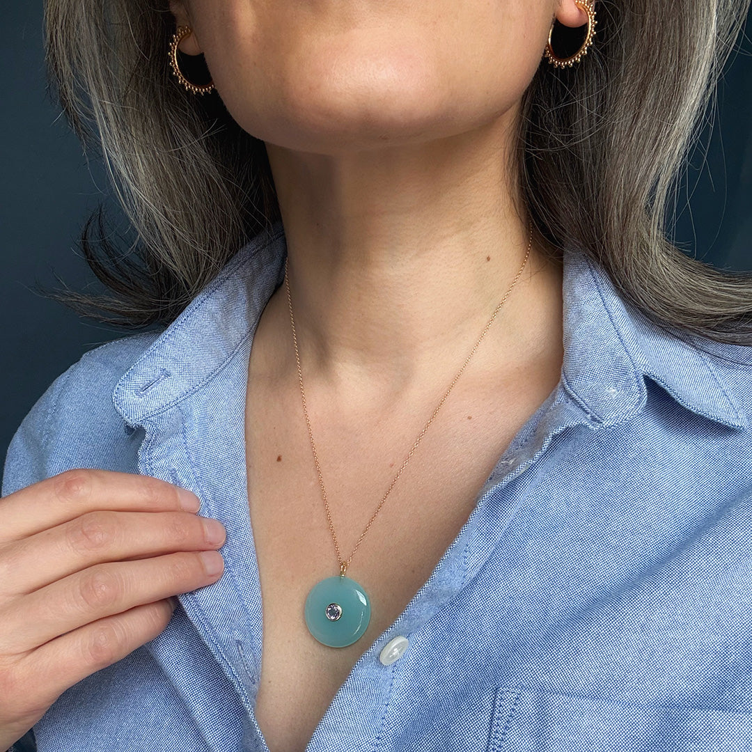 Close up of woman wearing a round chalcedony pendant on a gold chain