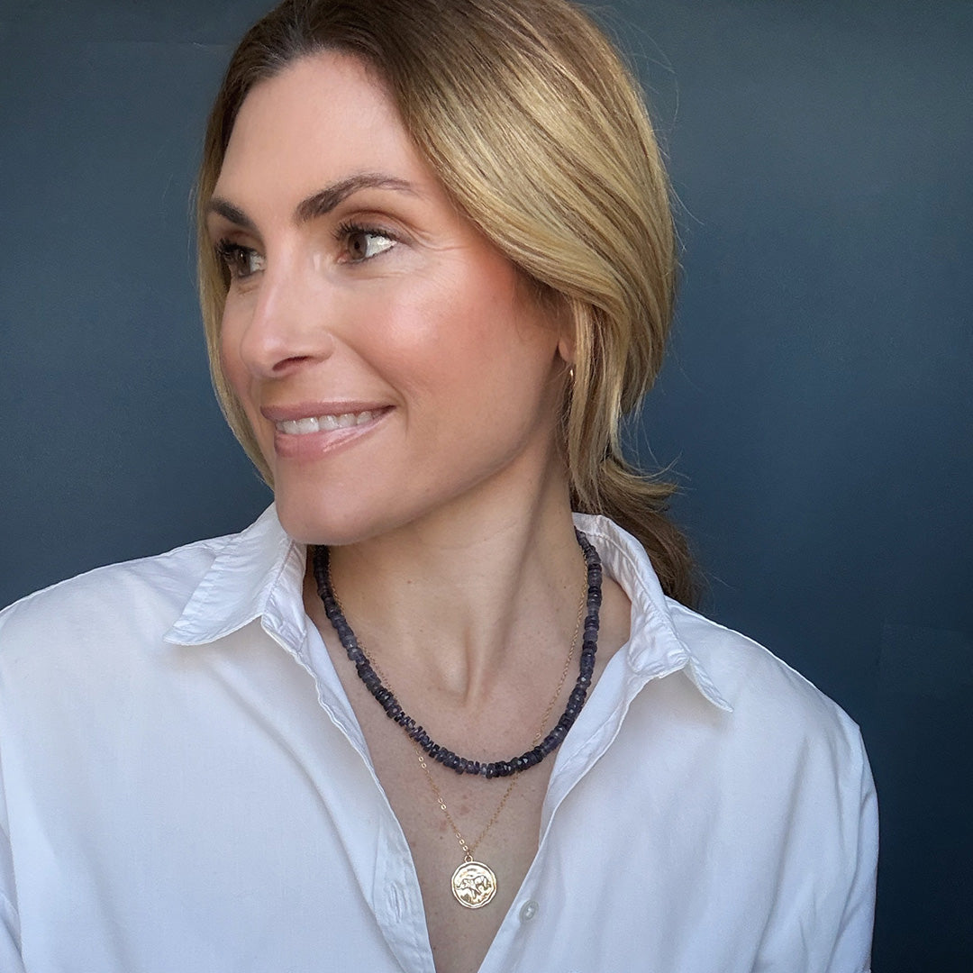 Woman wearing a gemstone necklace layered with a gold elephant pendant necklace