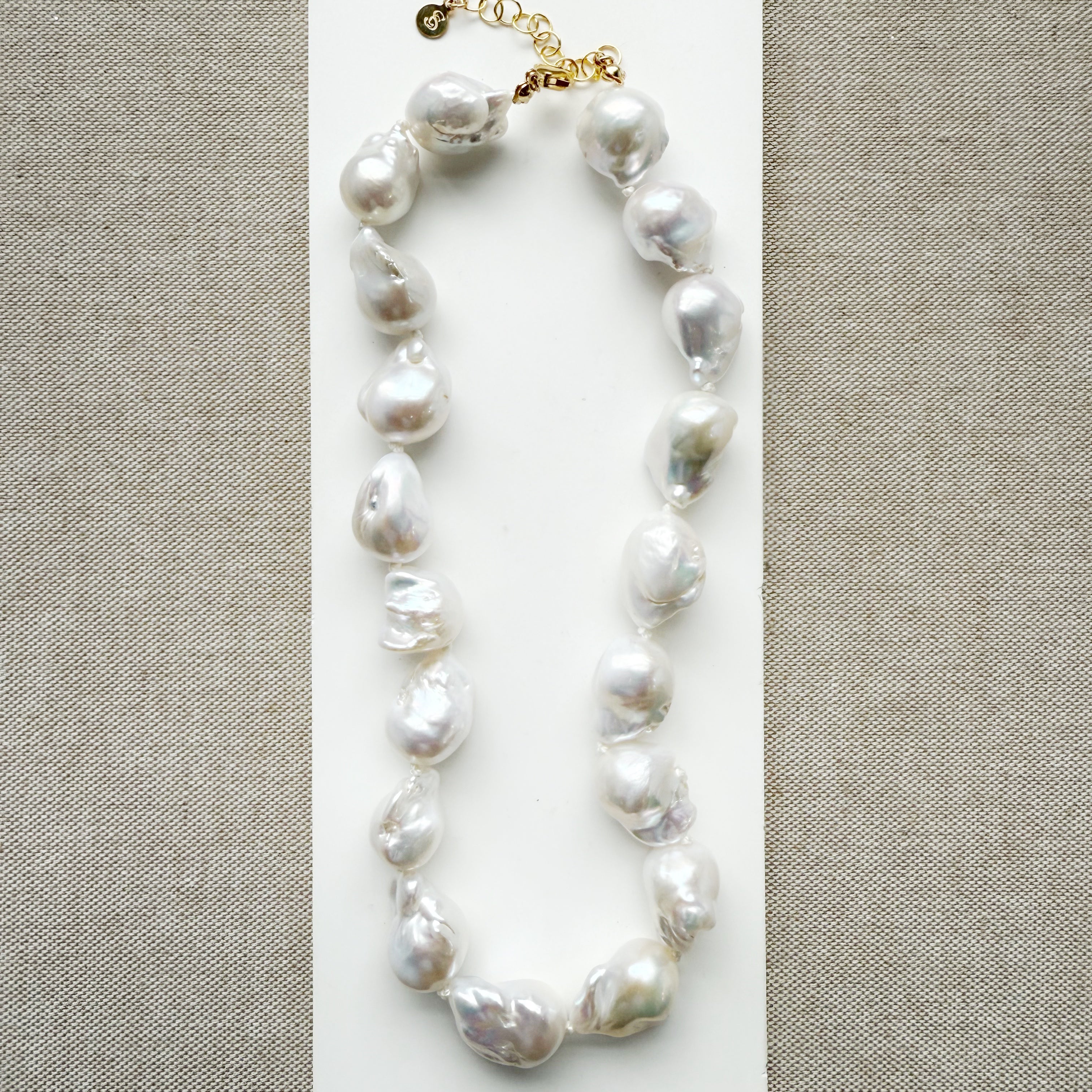Large baroque pearl necklace on a white card with a beige background