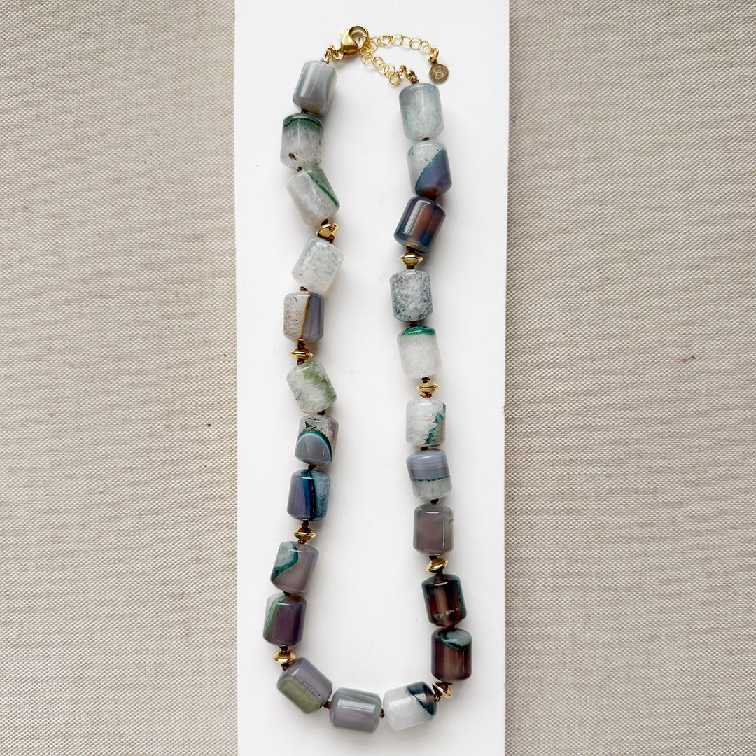 Necklace with multicolored green, brown ad gray agate beads on a beige background