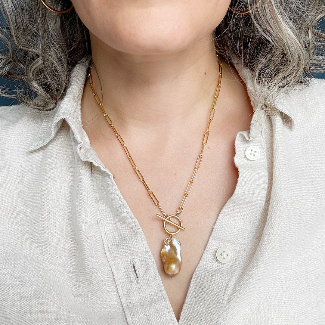 Person wearing gold necklace with large blush colored baroque pearl