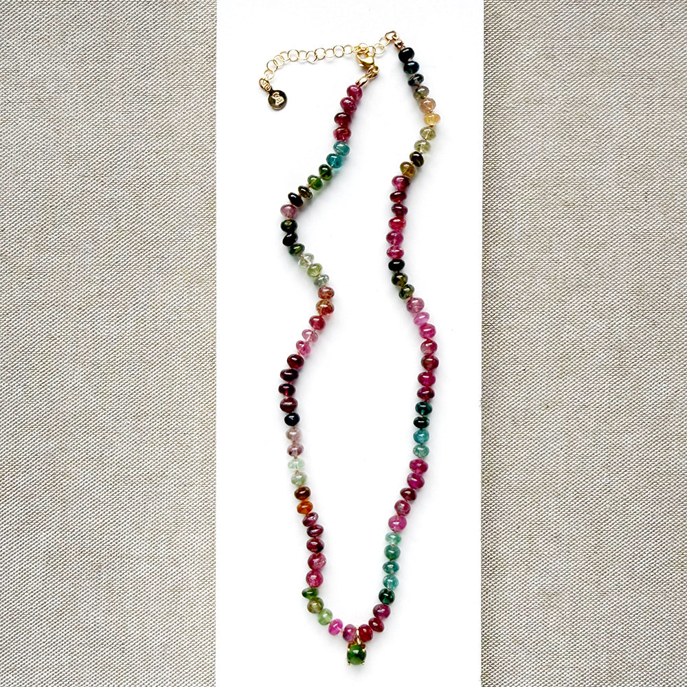 A smooth Watermelon Tourmaline beaded necklace in shades of pink, red, green, blue, and orange, featuring a small green tourmaline charm on a white card.