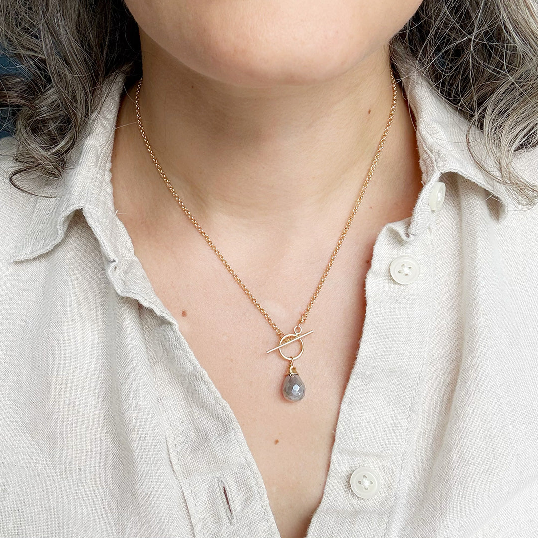 Person wearing gold necklace with toggle and moonstone drop