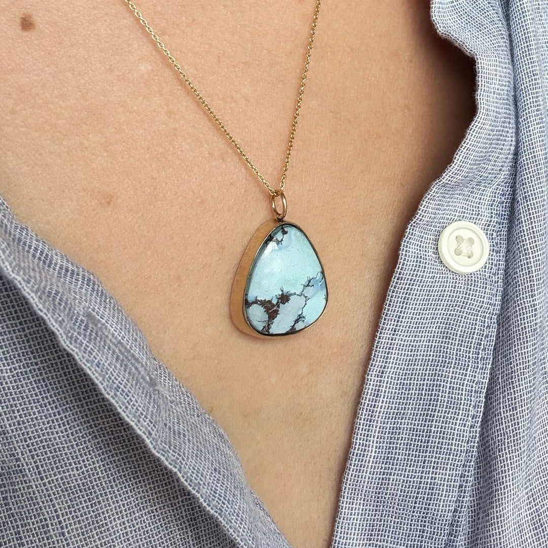 Necklace with a Golden Hills turquoise pendant worn by a person wearing a light blue shirt.