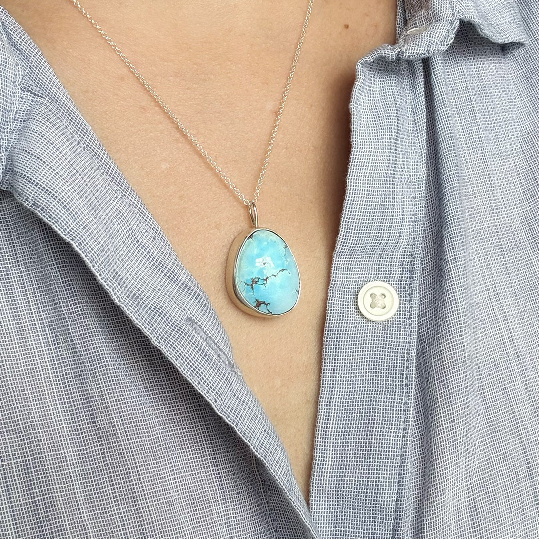 Person wearing a light blue shirt with a Golden Hills turquoise pendant necklace.