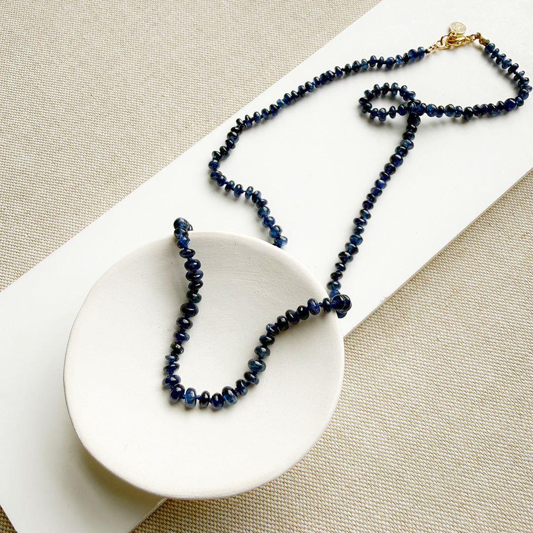 Knotted necklace with smooth sapphire gemstones in a white dish
