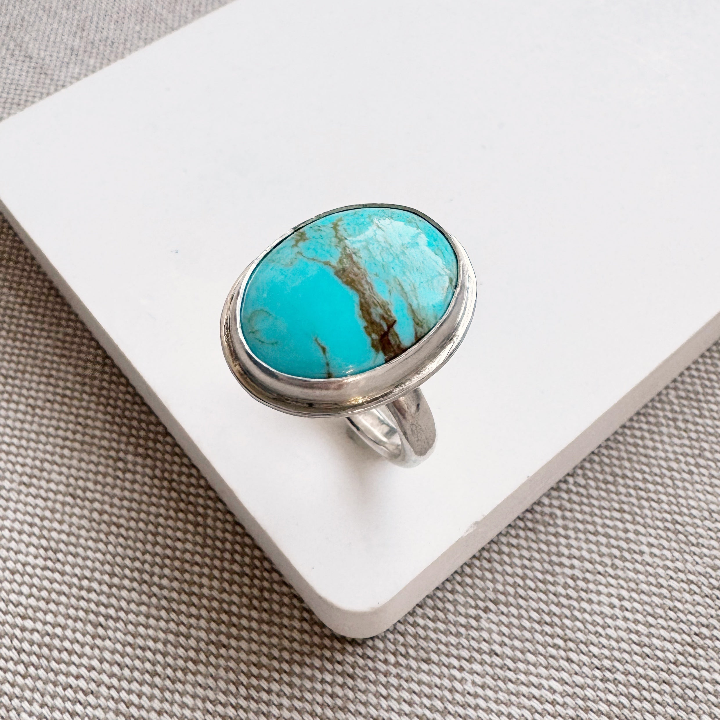 Turquoise ring on a white stand with a gray textured background