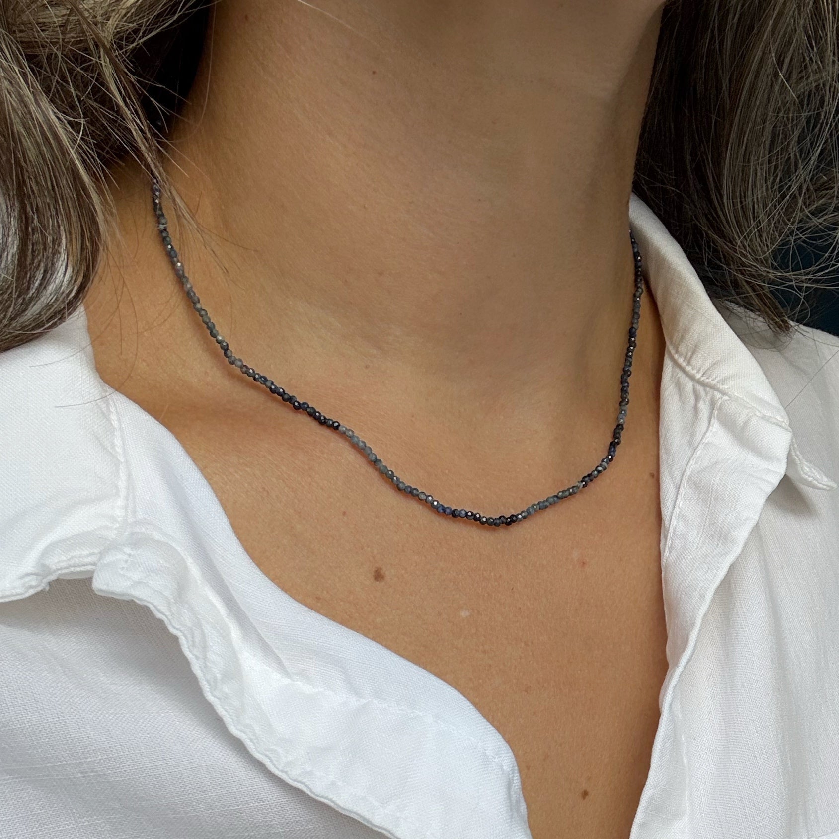 Person wearing a white shirt with a sapphire gemstone necklace