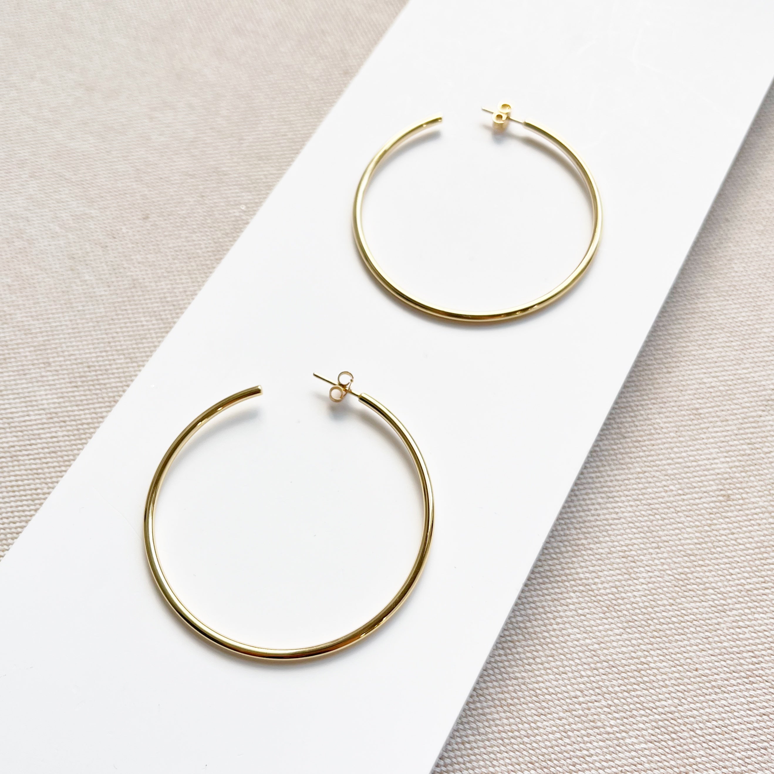 Oversized gold hoop earrings on a white surface with a neutral background