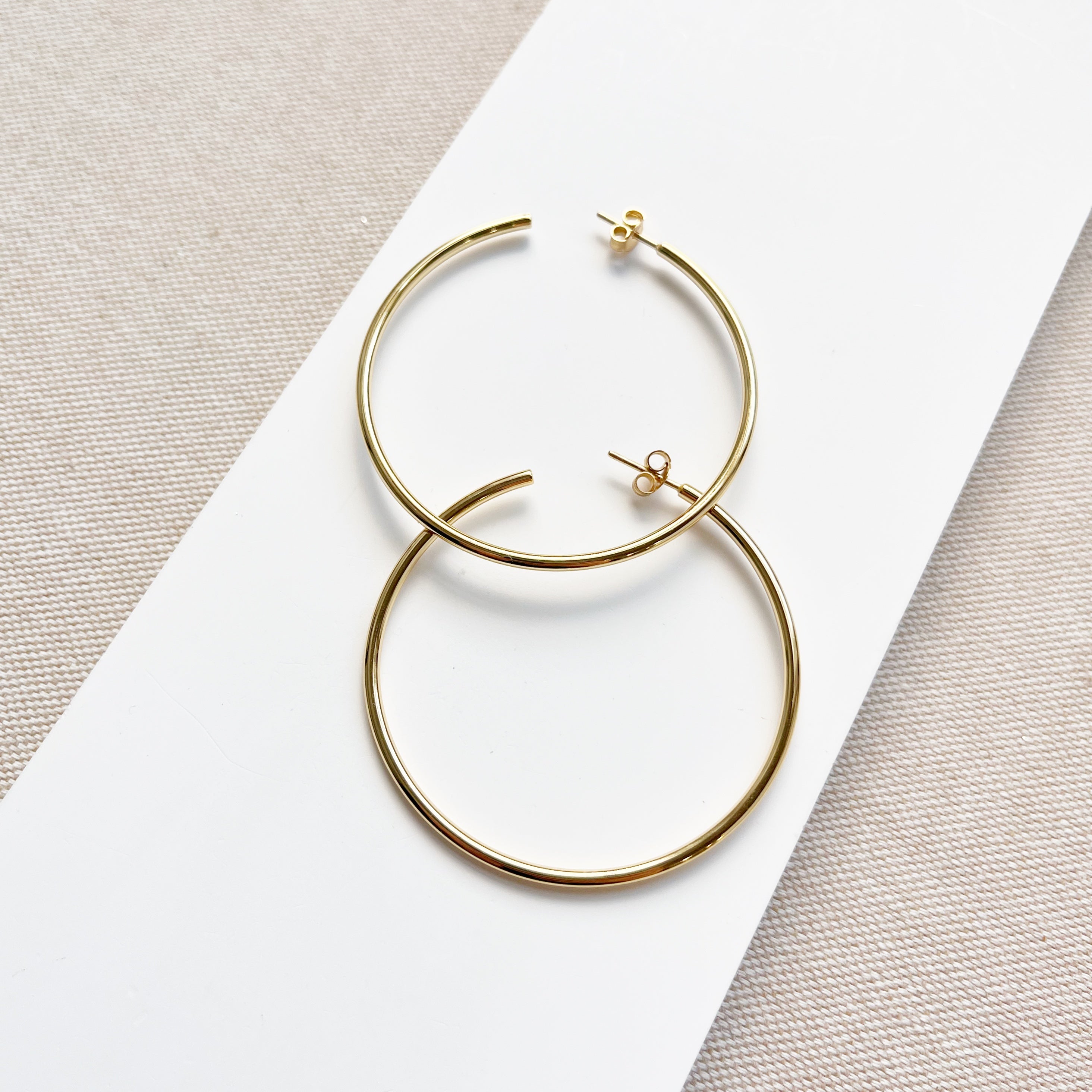 Oversized gold hoop earrings on a white surface with a beige background