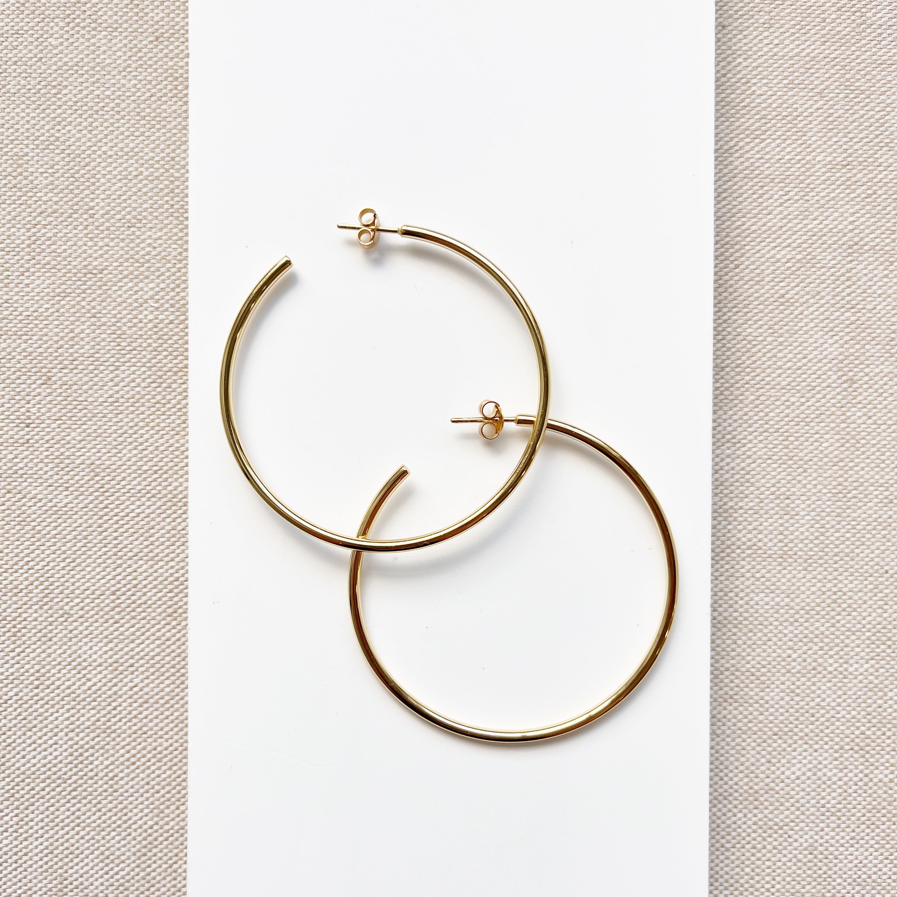 Oversized gold hoop earrings on a light beige fabric background