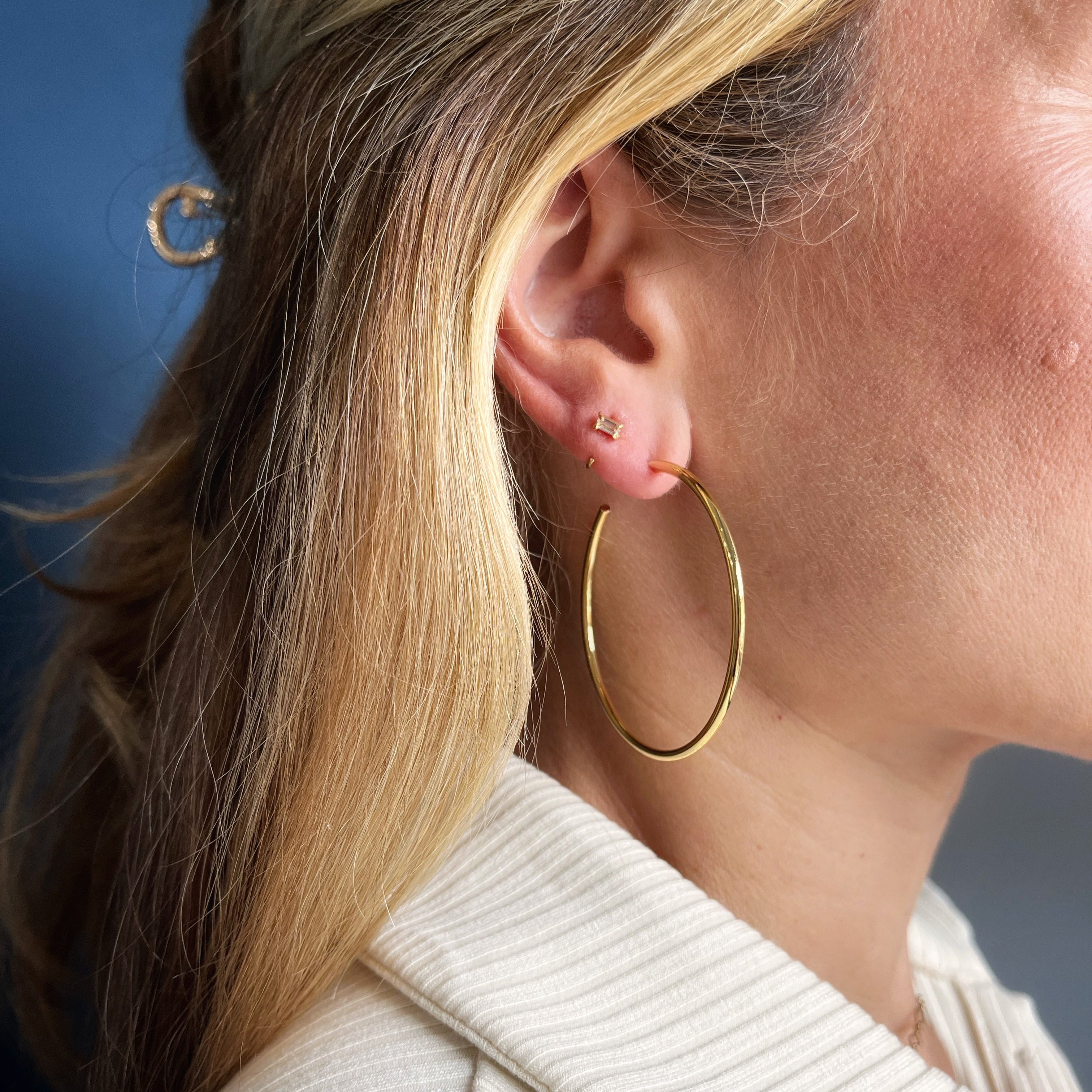 Close-up of a person wearing gold hoop earrings with a neutral background