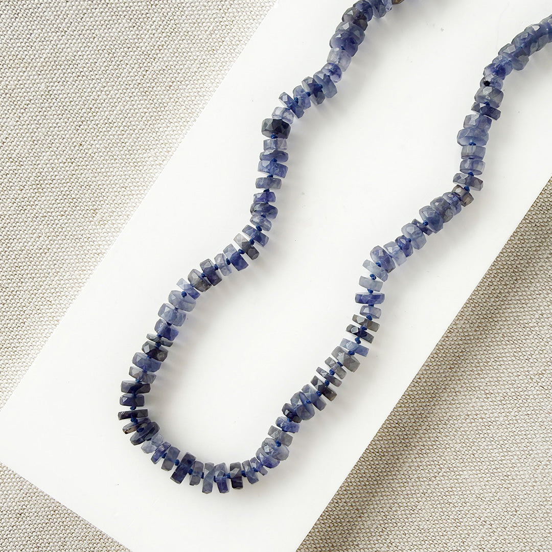 Iolite gemstone necklace on a white dish with a beige fabric background