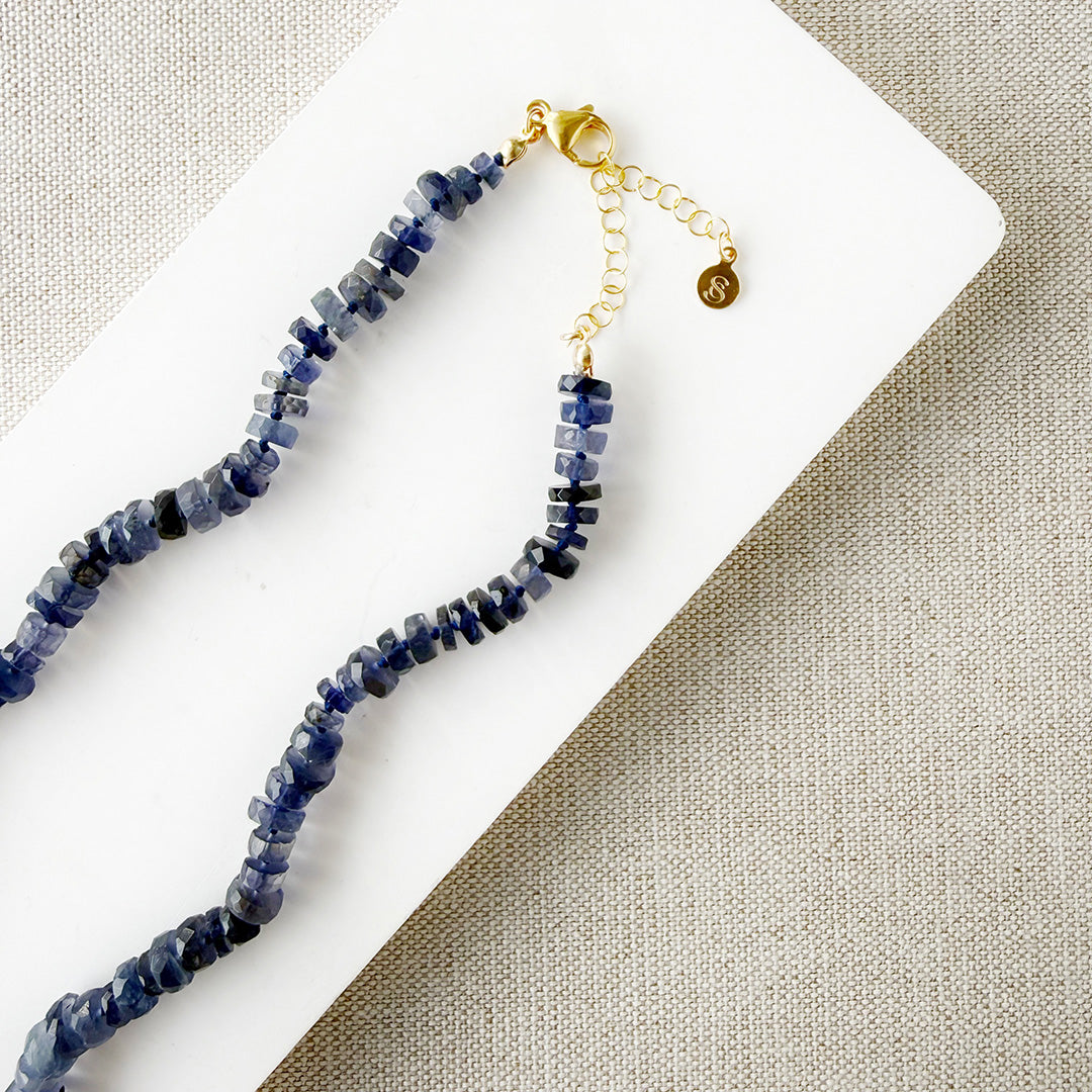 Iolite gemstone necklace on a white dish with a beige fabric background