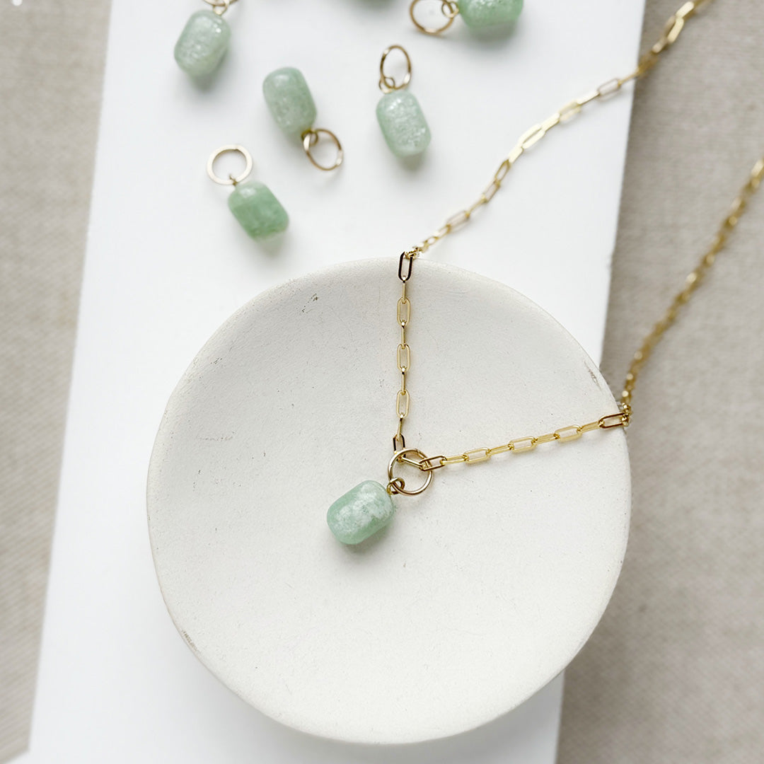 Jade charm in a cylinder cut on a gold chain in a white dish