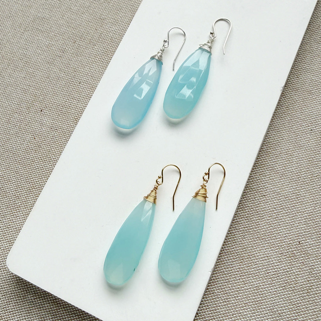 Pair of blue chalcedony teardrop earrings on a white card with a textured background