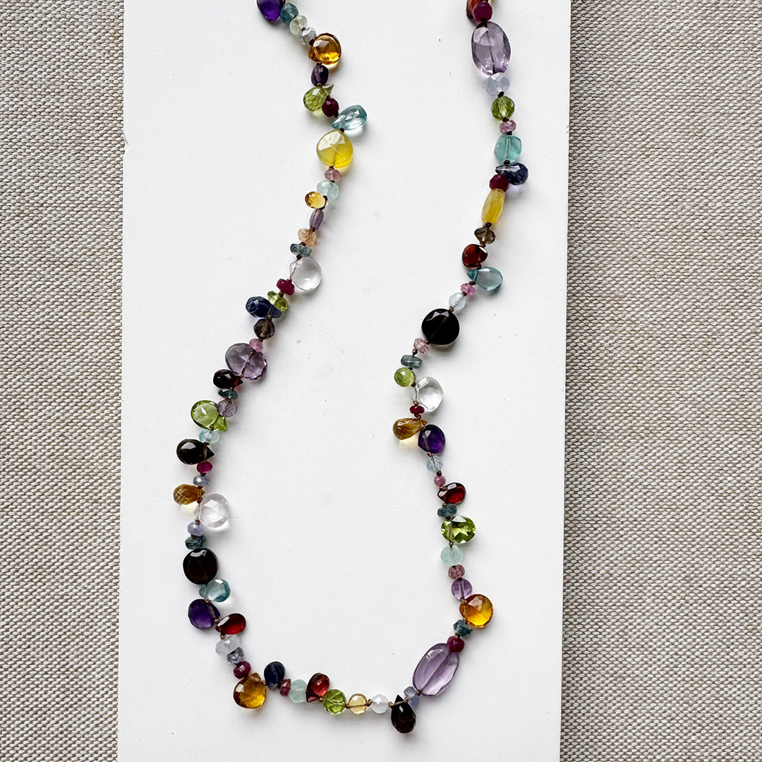Multicolored gemstone necklace on a white card with a gray background