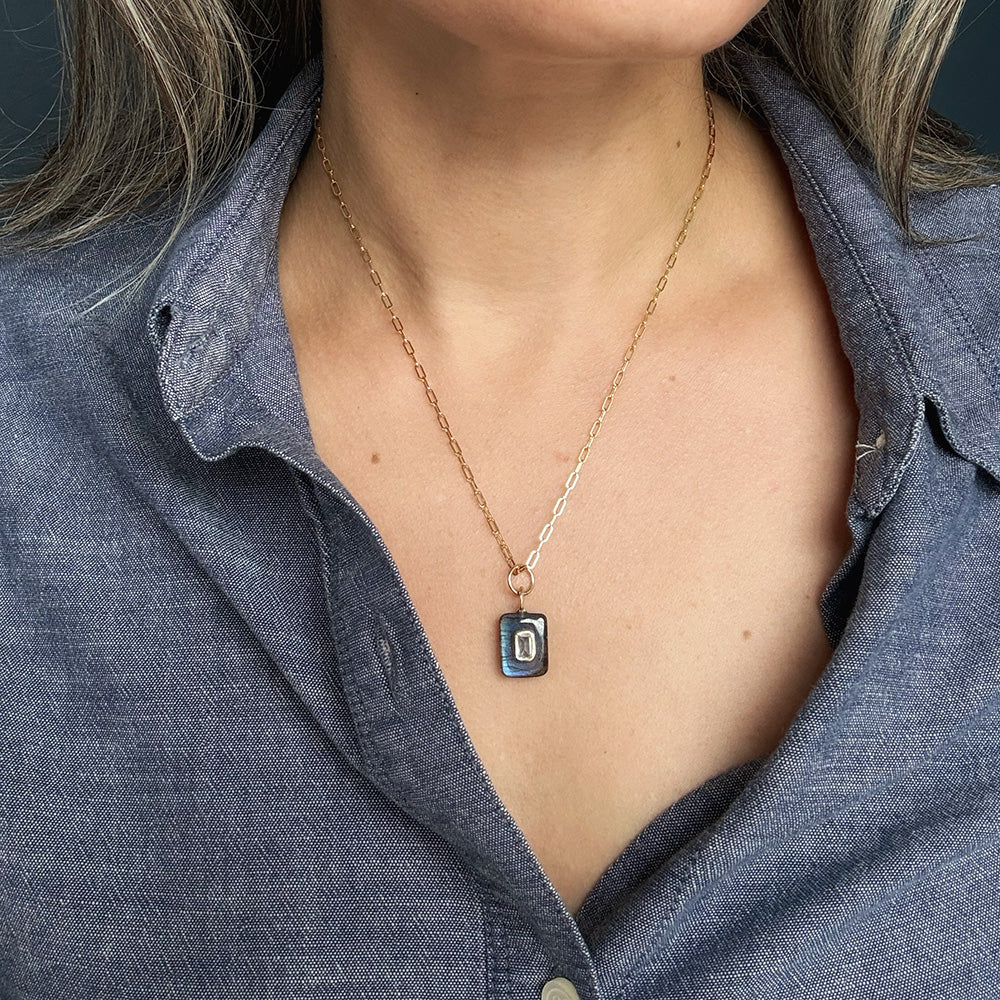 Woman wearing ectangular labradorite charm with inset cz stone on a gold chain