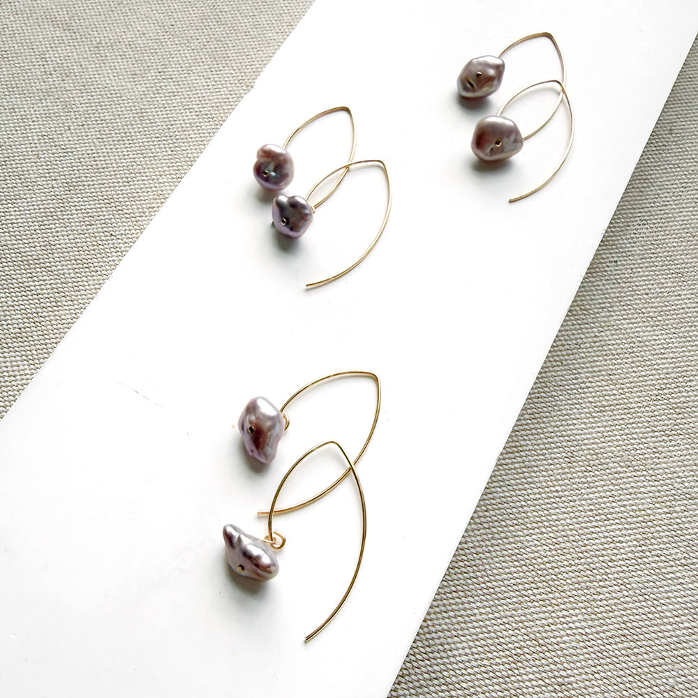 Irregular lavender pearl on a gold v-wire earring, displayed on a white card