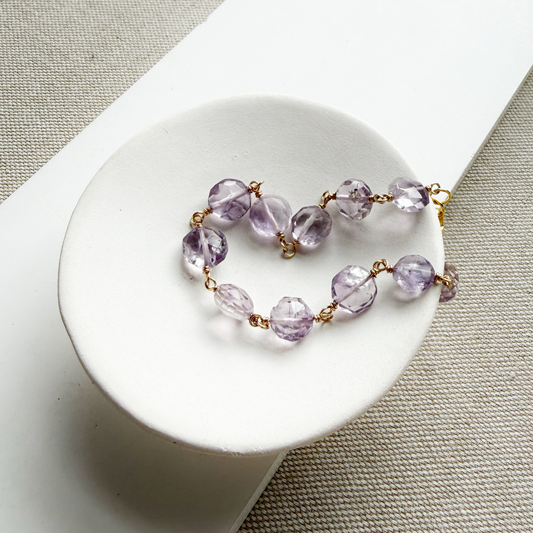 Amethyst bracelet with gold accents in a white dish against a beige background