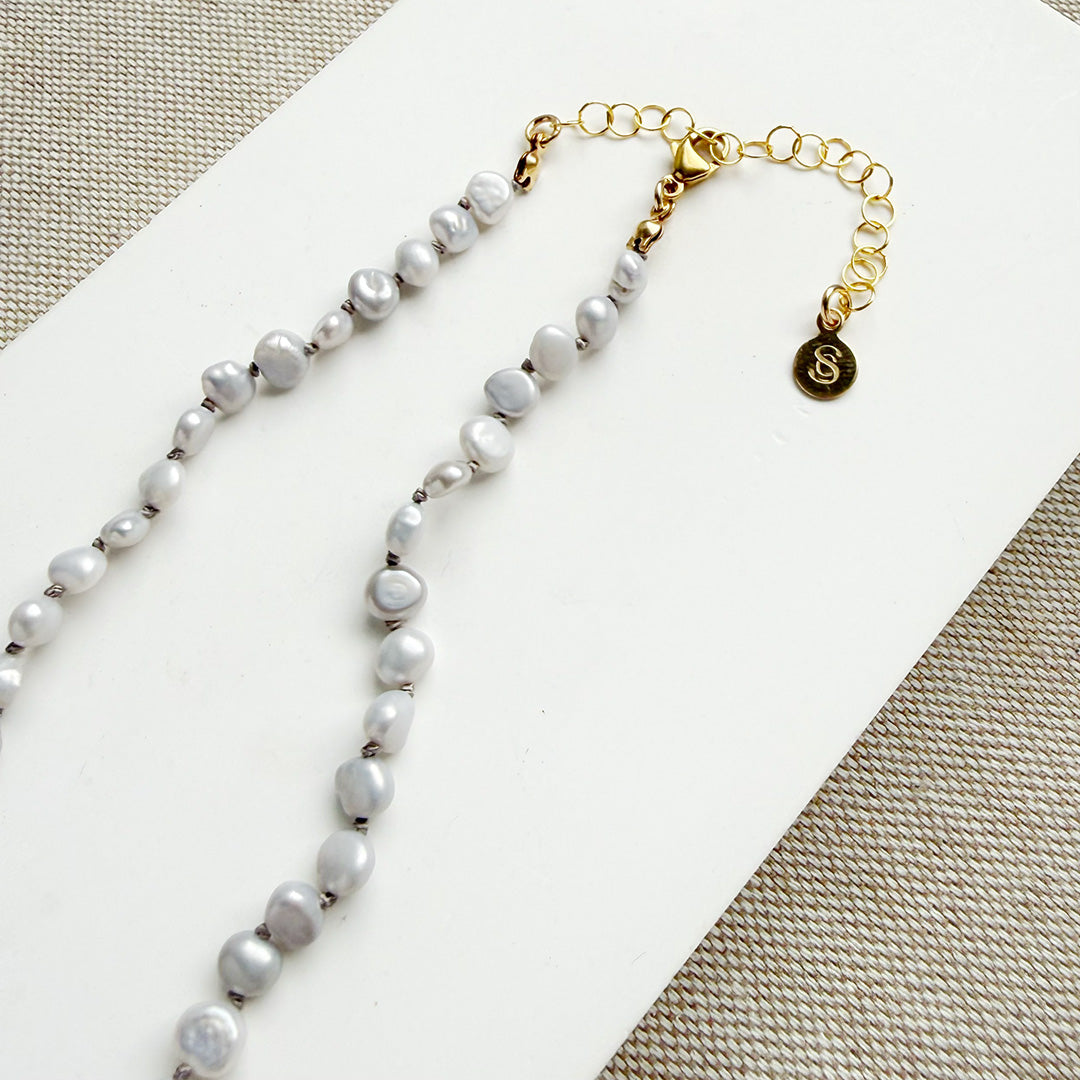 Pearl necklace with gold clasp on a light gray background