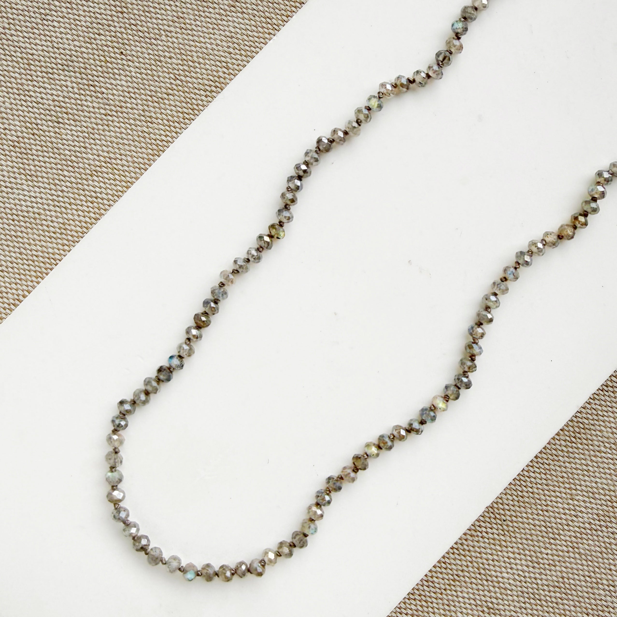 Small labradorite gems knotted necklace on a white surface with a beige background