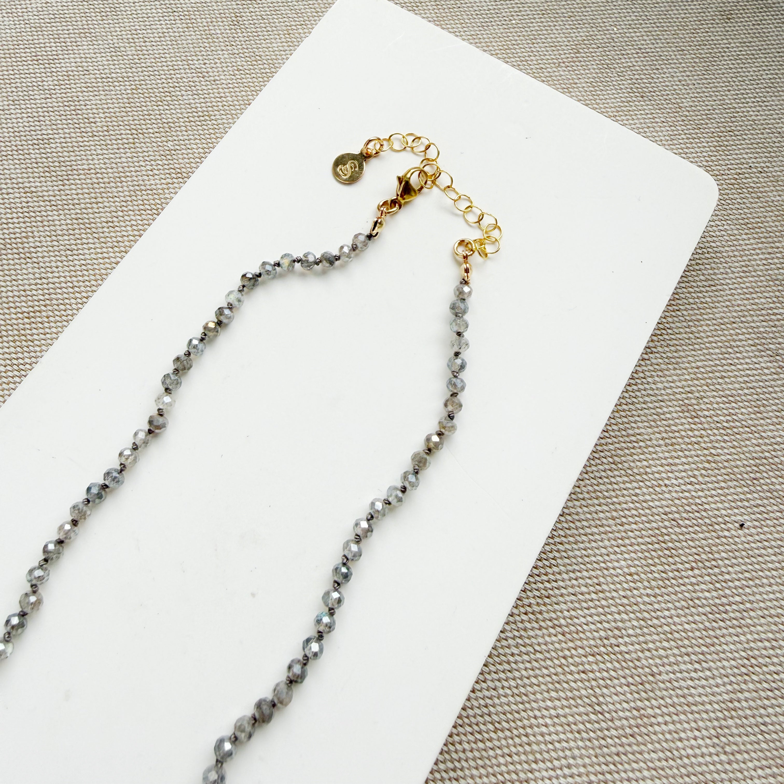 Clasp and extender for a small labradorite gems knotted necklace on a white surface with a beige background