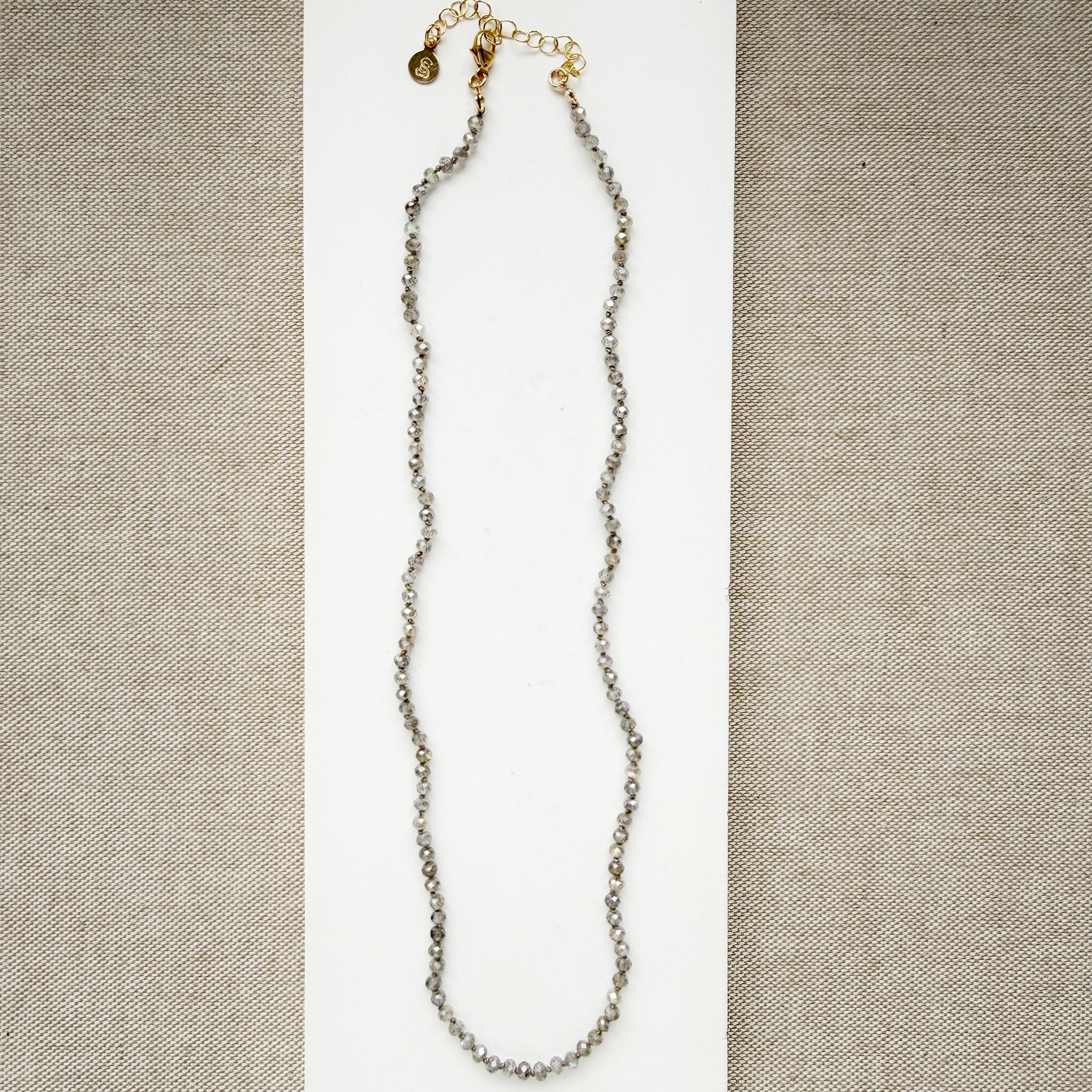 Small labradorite gems knotted necklace on a white surface with a beige background