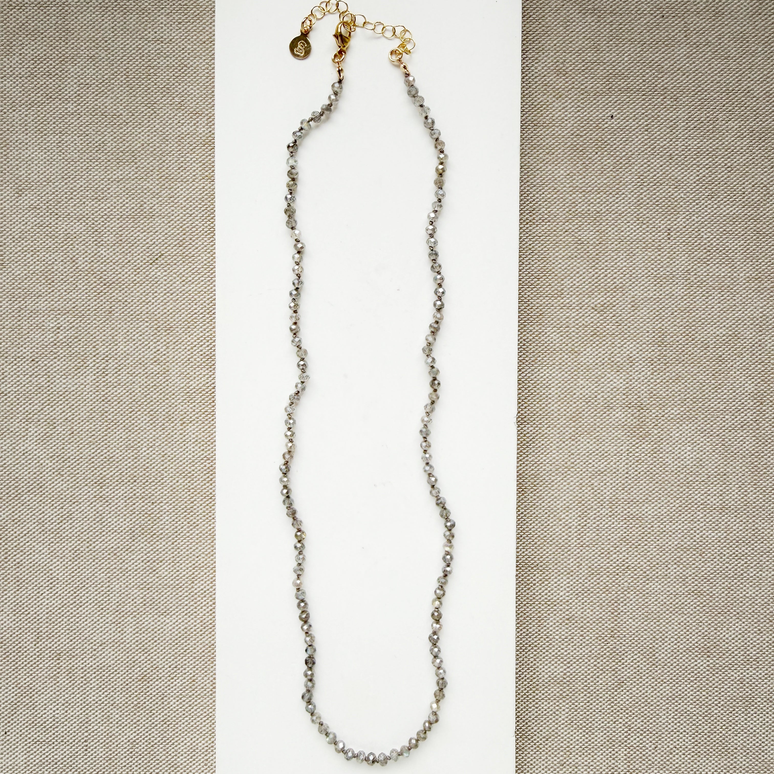 Small labradorite gems knotted necklace on a white surface with a beige background