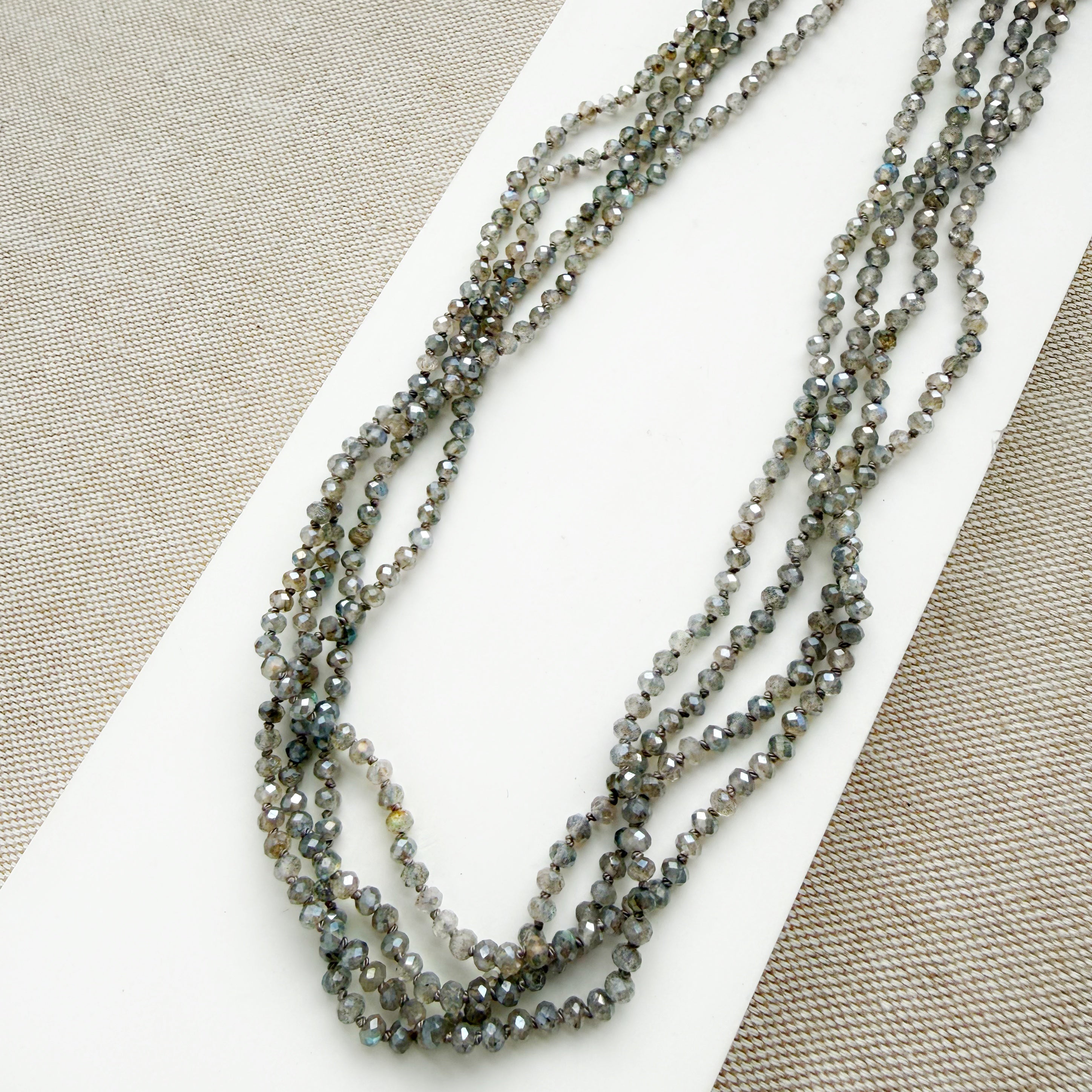 Small labradorite gems knotted necklace on a white surface with a beige background