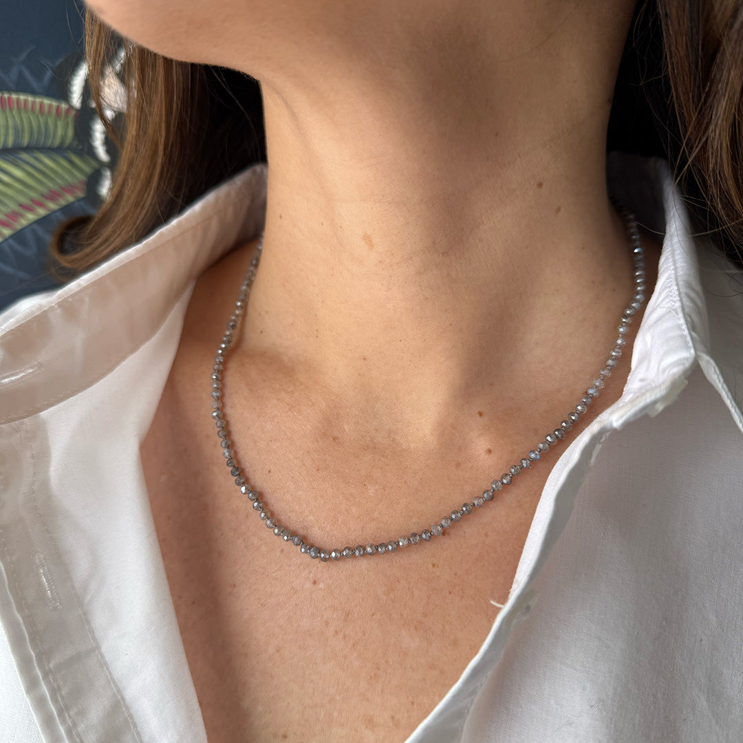 Small knotted labradorite necklace worn by a person with a white shirt and patterned background