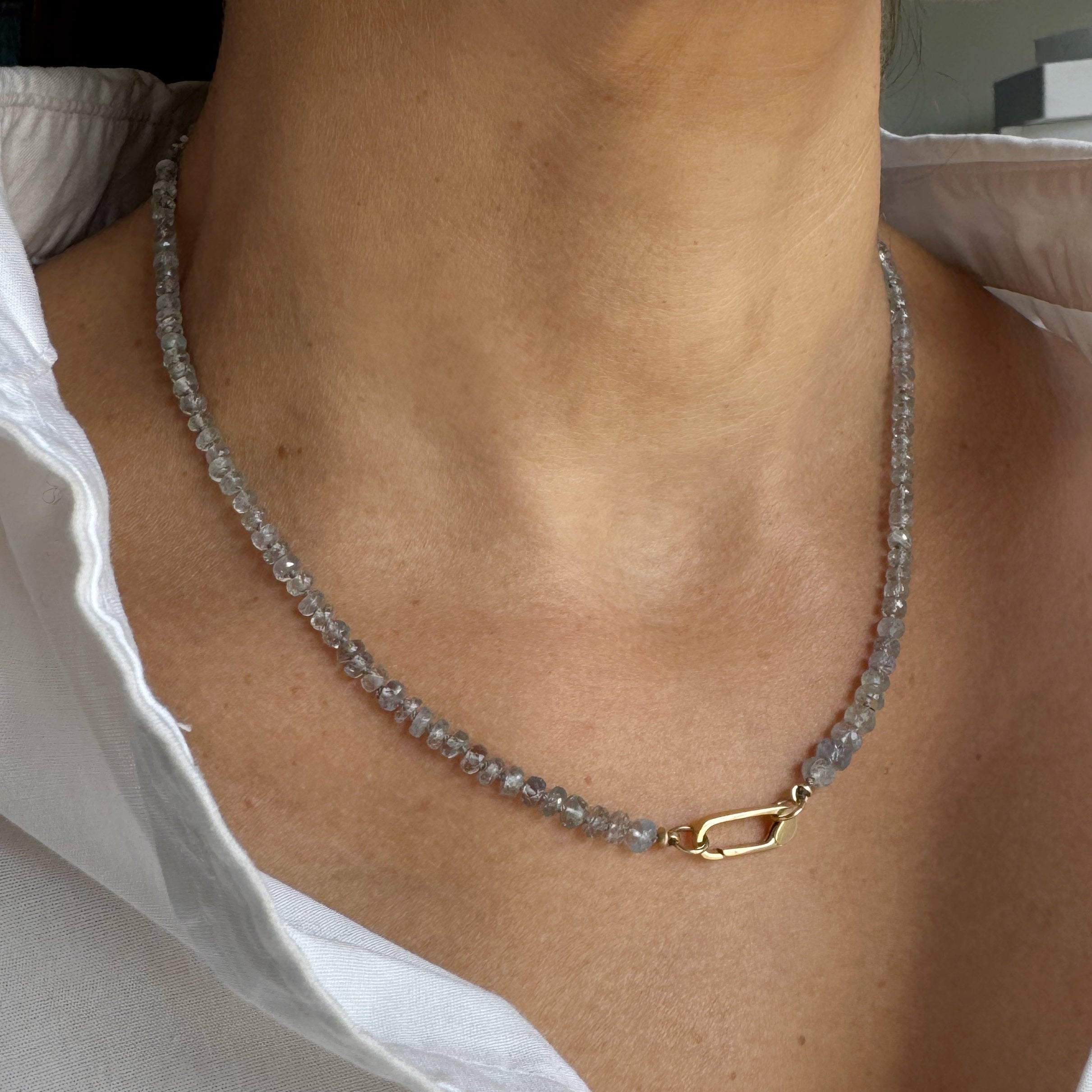 Necklace with a gold clasp worn by a person wearing a white shirt.