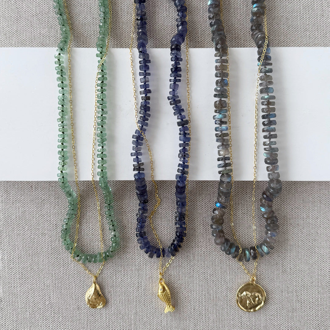Gemstone necklaces layered with gold chains with charm pendants
