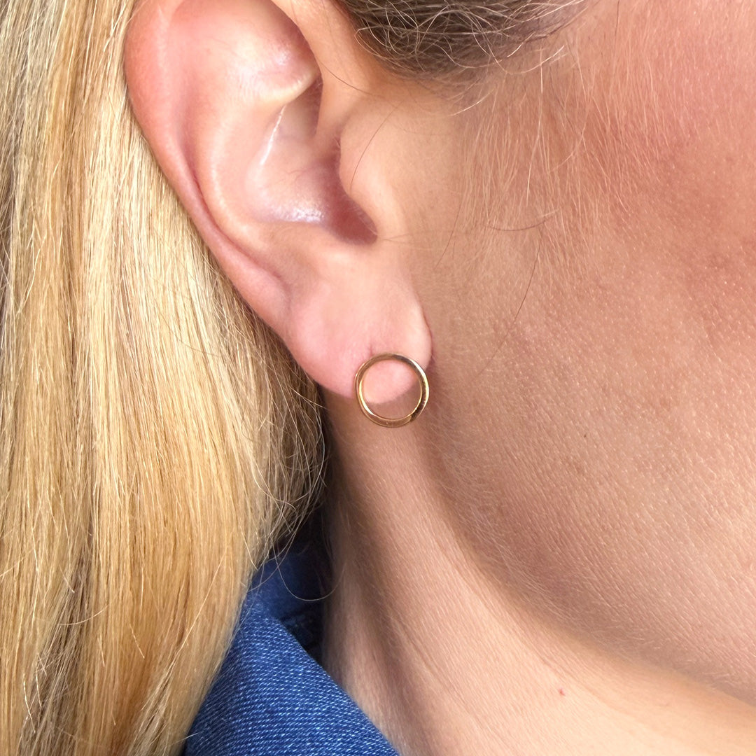 Close-up of a person wearing a gold circle stud with a blue denim shirt.