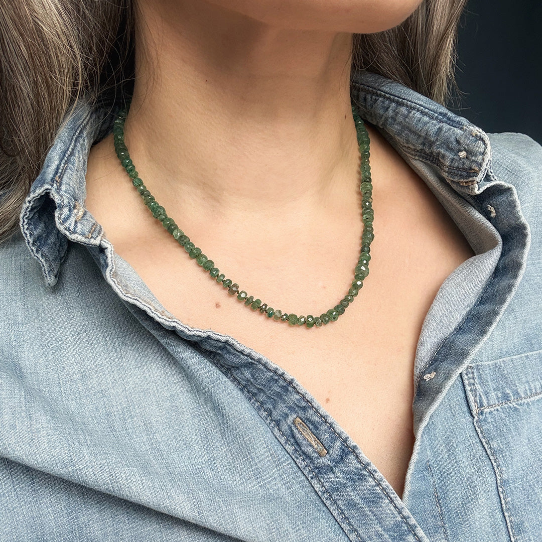 Person wearing a green kyanite gemstone necklace with a denim shirt