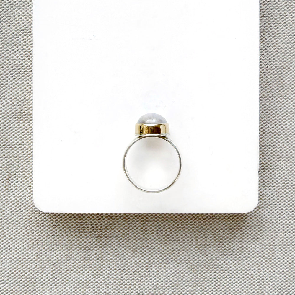 Side view of round moonstone mixed metal ring on a white background