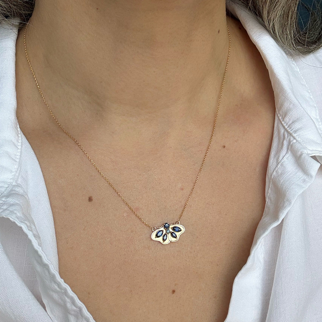 Necklace with a moth pendant worn by a person in a white shirt.