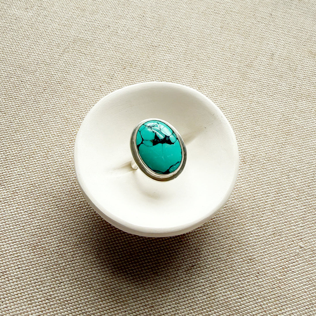 White ceramic dish with a Nevada turquoise ring on a beige fabric background