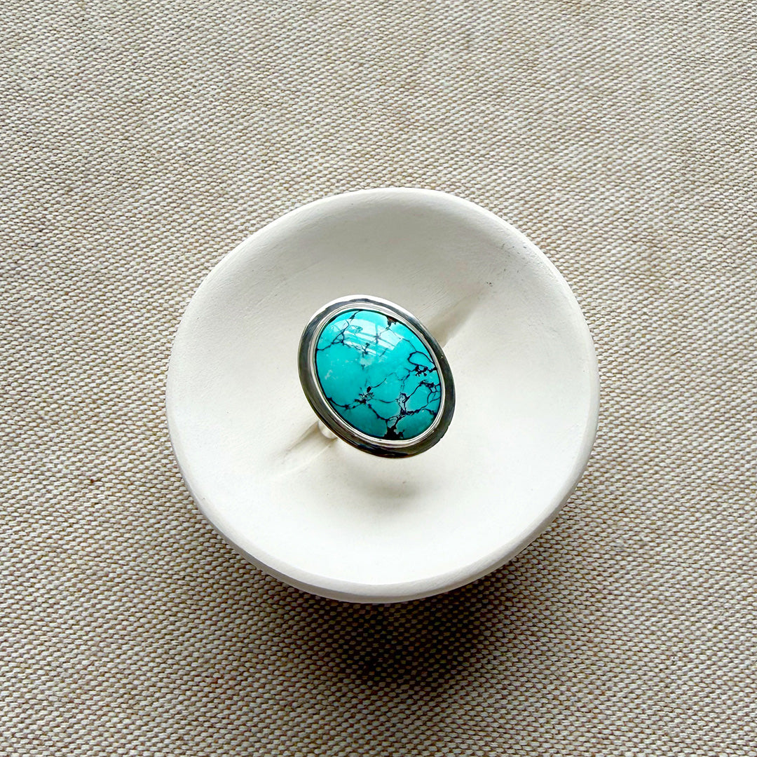 White ceramic dish with a Nevada turquoise ring on a beige fabric background