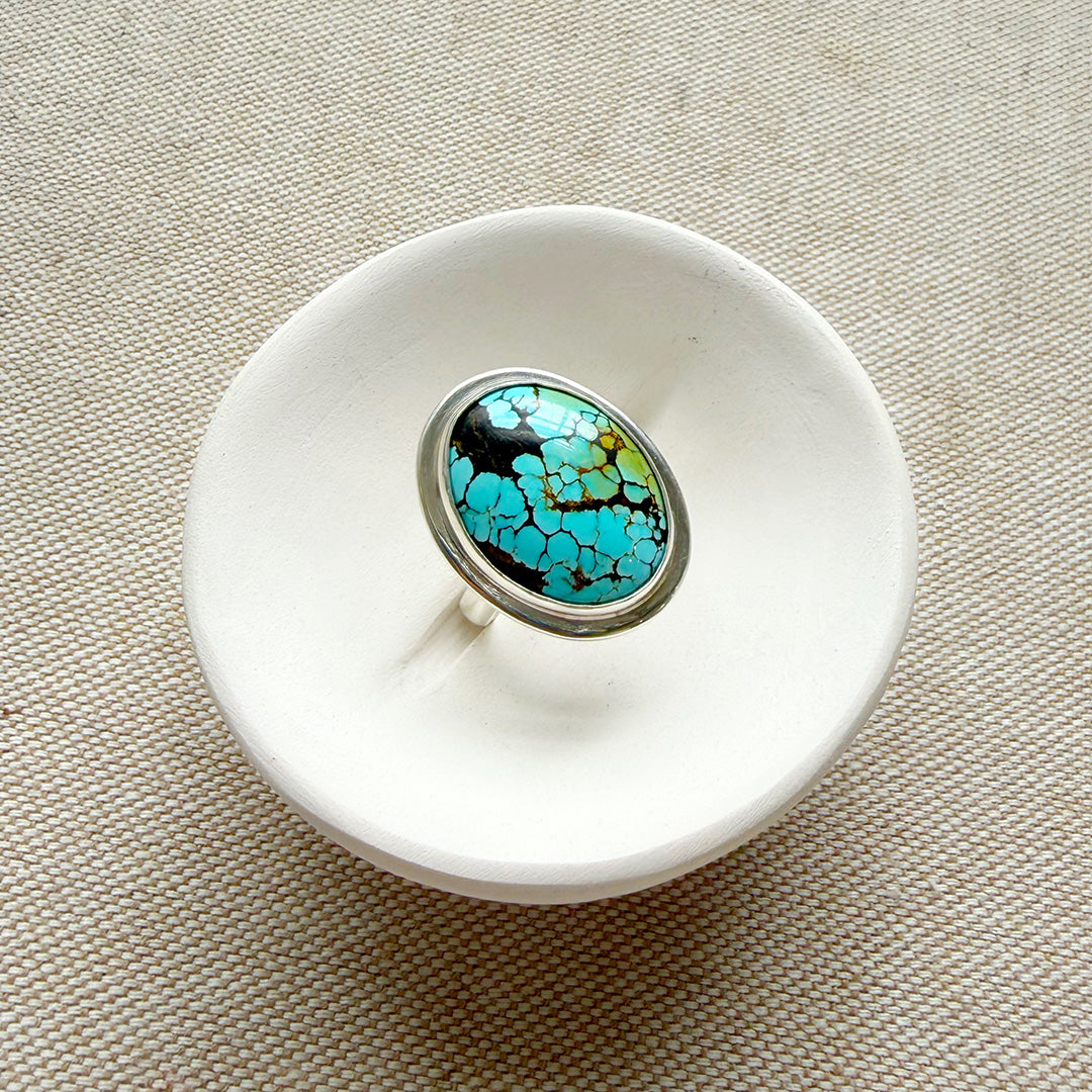 White ceramic dish with a Nevada turquoise ring on a beige fabric background