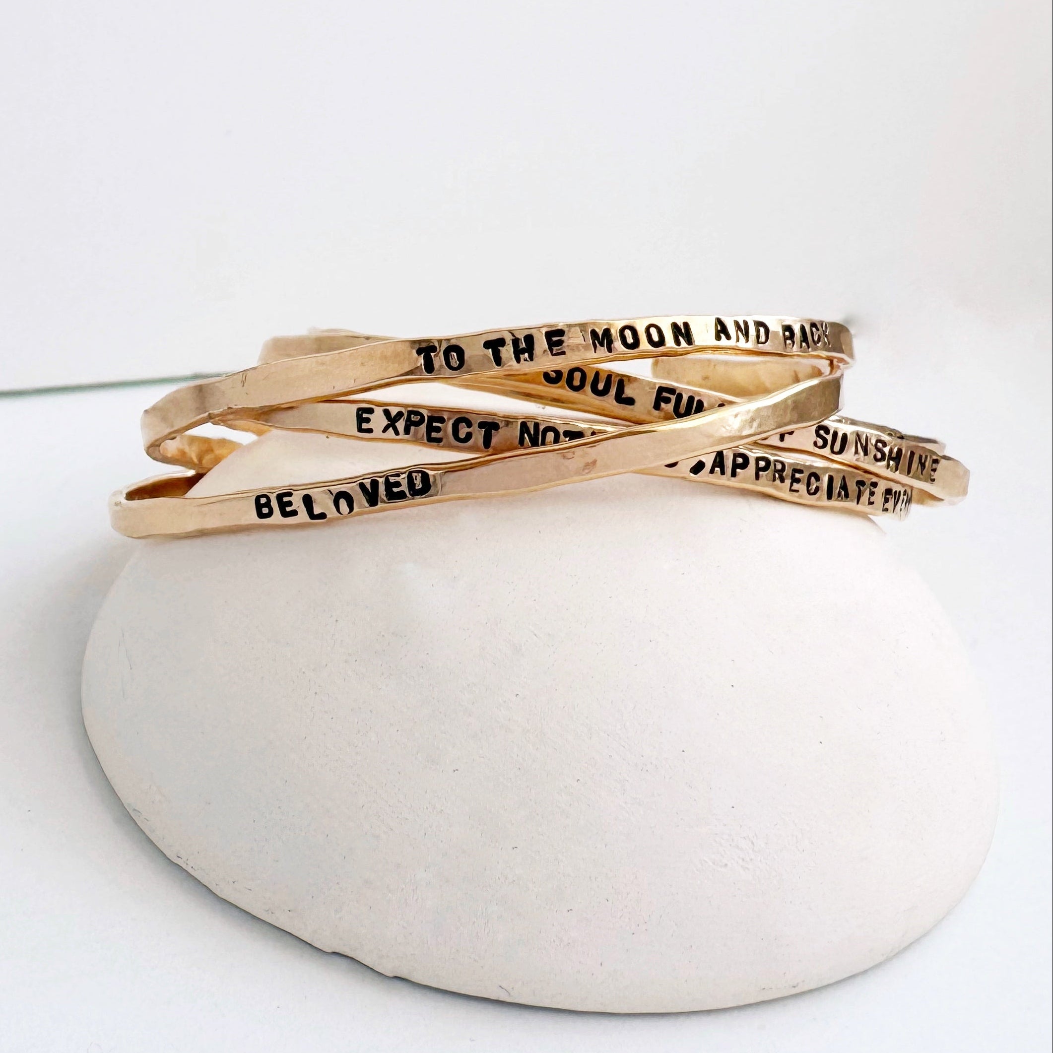 Set of gold bracelets with motivational phrases on a white surface