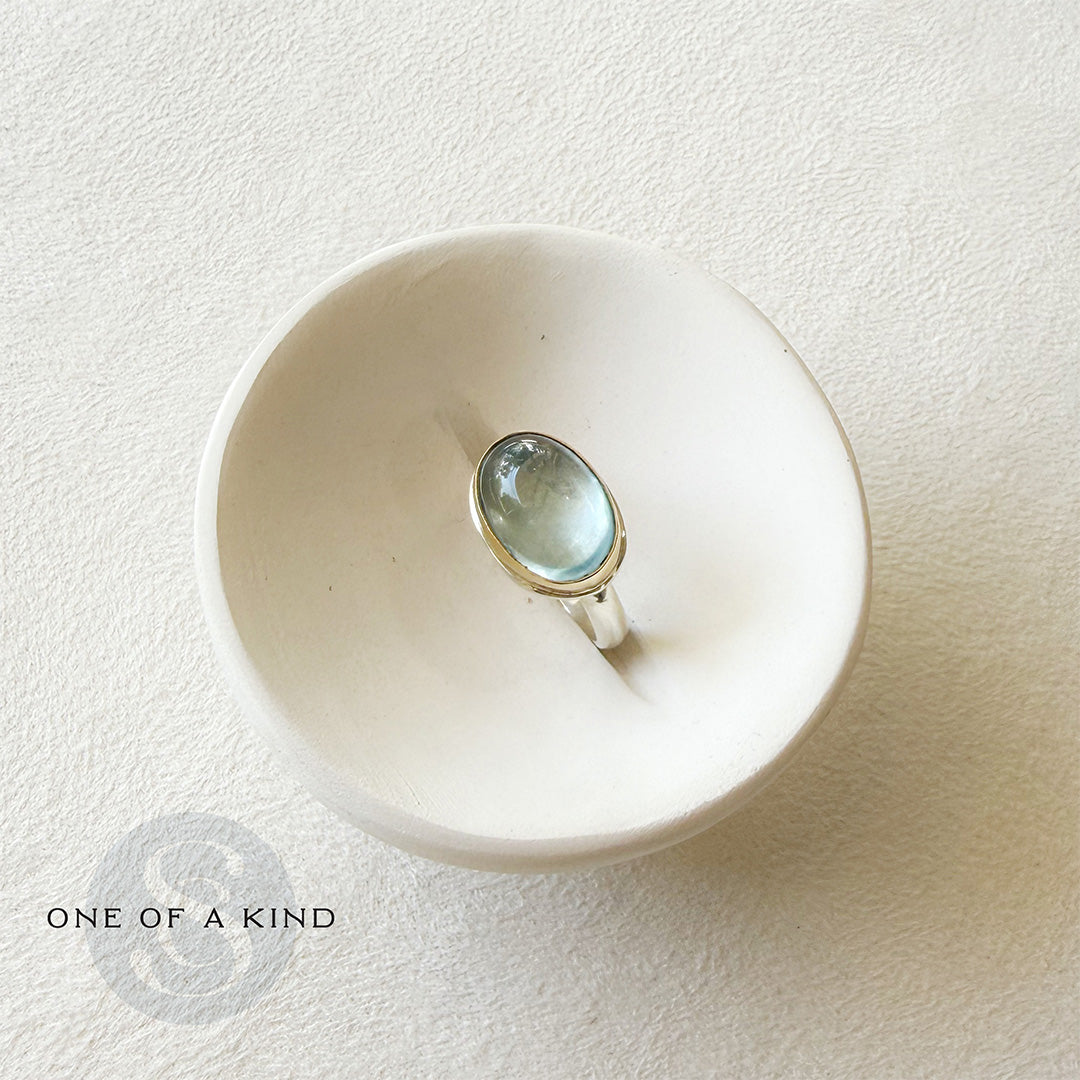 Oval aquamarine mixed metal ring in a white dish with one of a kind icon