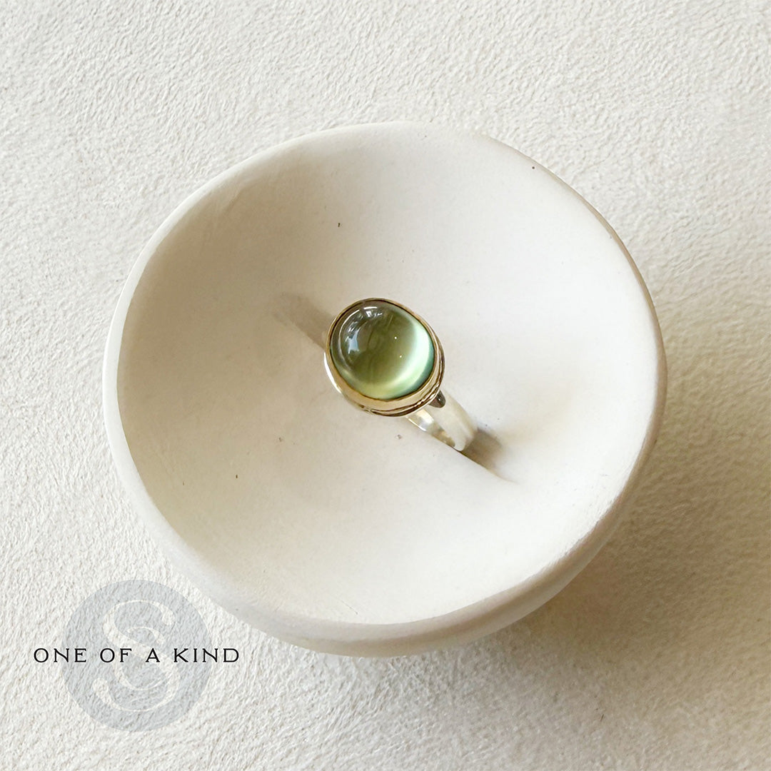 Ring with a green prehnite gemstone in a white dish on a textured beige background