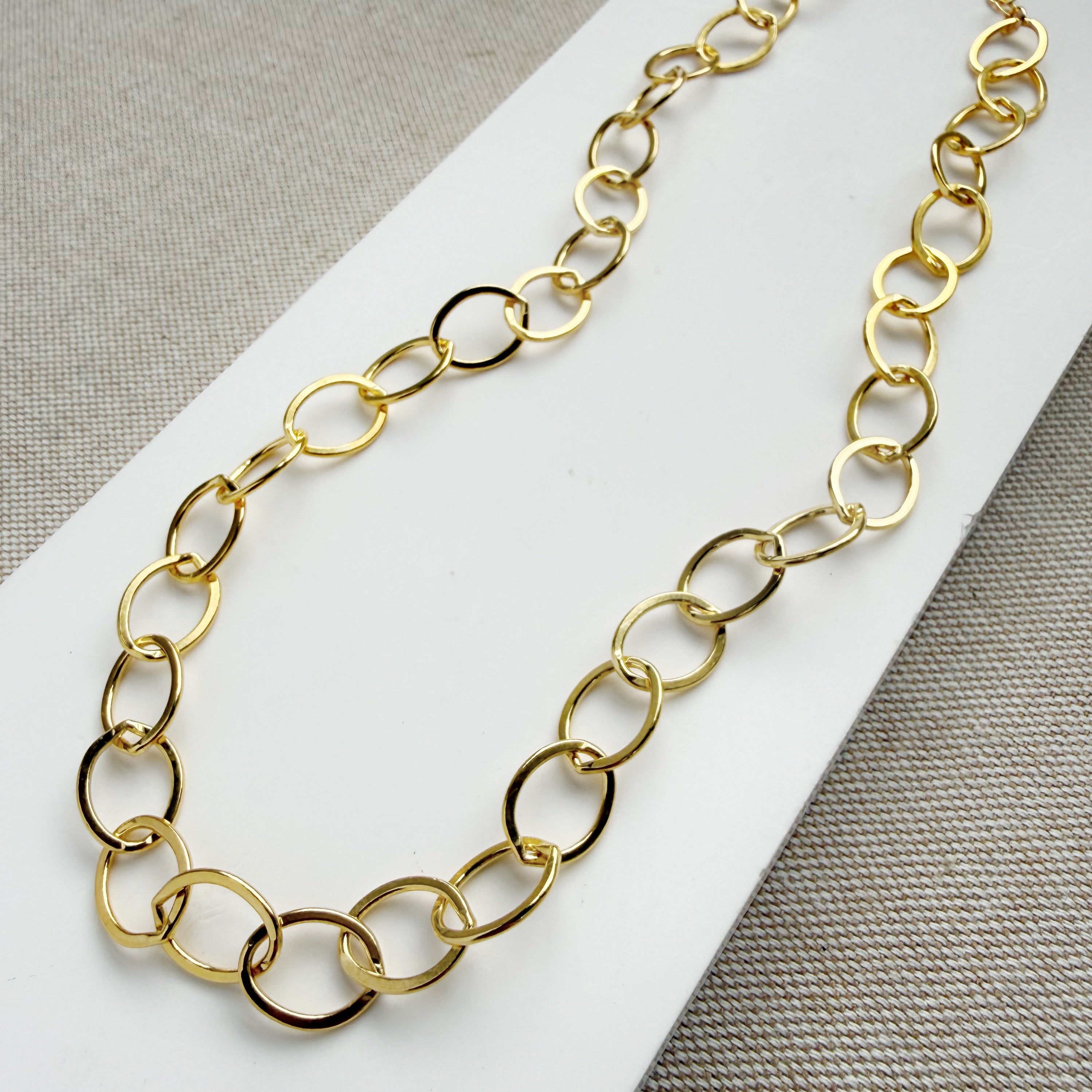 Chunky gold chain necklace on a white card with a gray background
