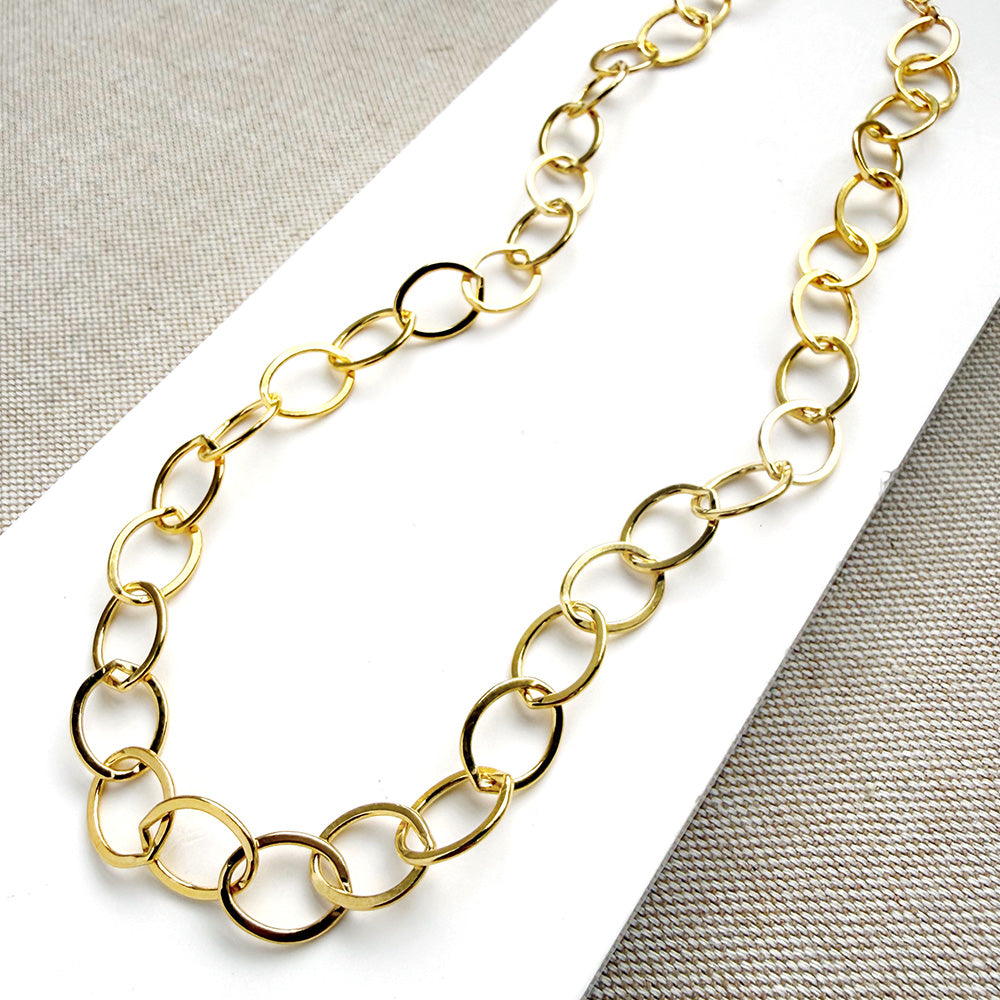 Chunky gold chain necklace on a white card with a gray background
