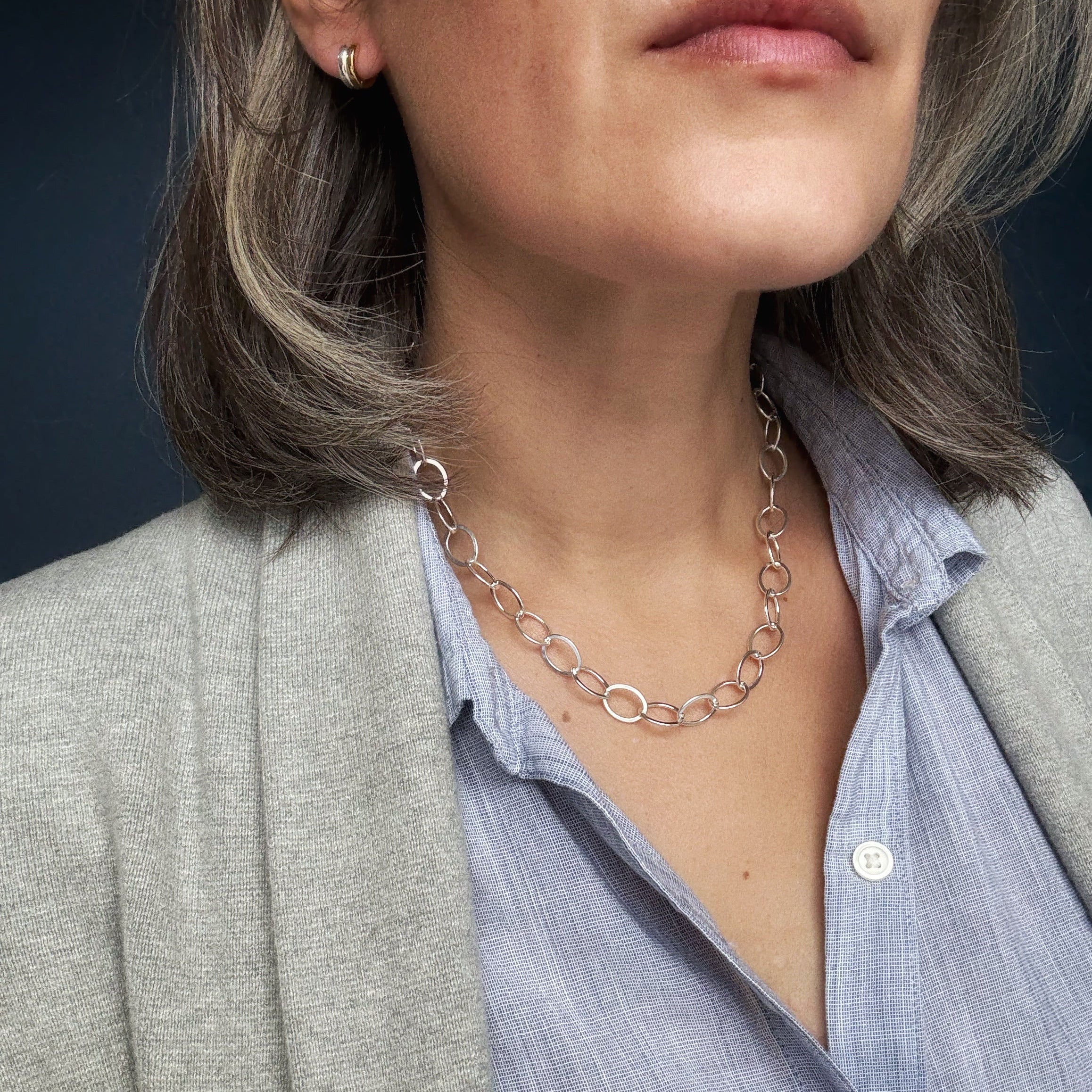 Close-up of a person wearing a chunky silver chain necklace against a dark background